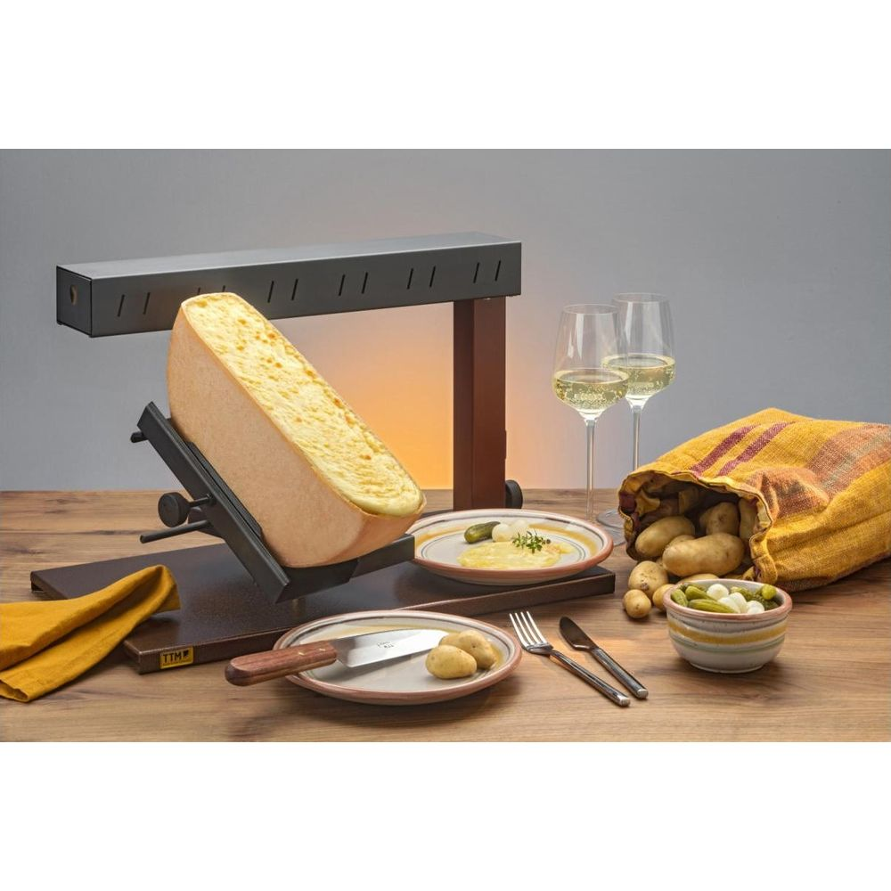 Ein Raclette-Käse wird über einem Gerät geschmolzen. Kartoffeln und Gläser daneben.