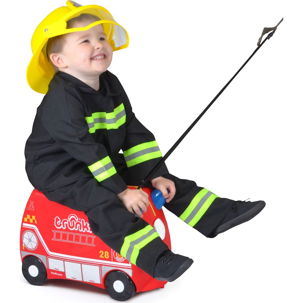 Un bambino con un costume completo da vigile del fuoco siede su un camioncino dei pompieri giocattolo rosso.