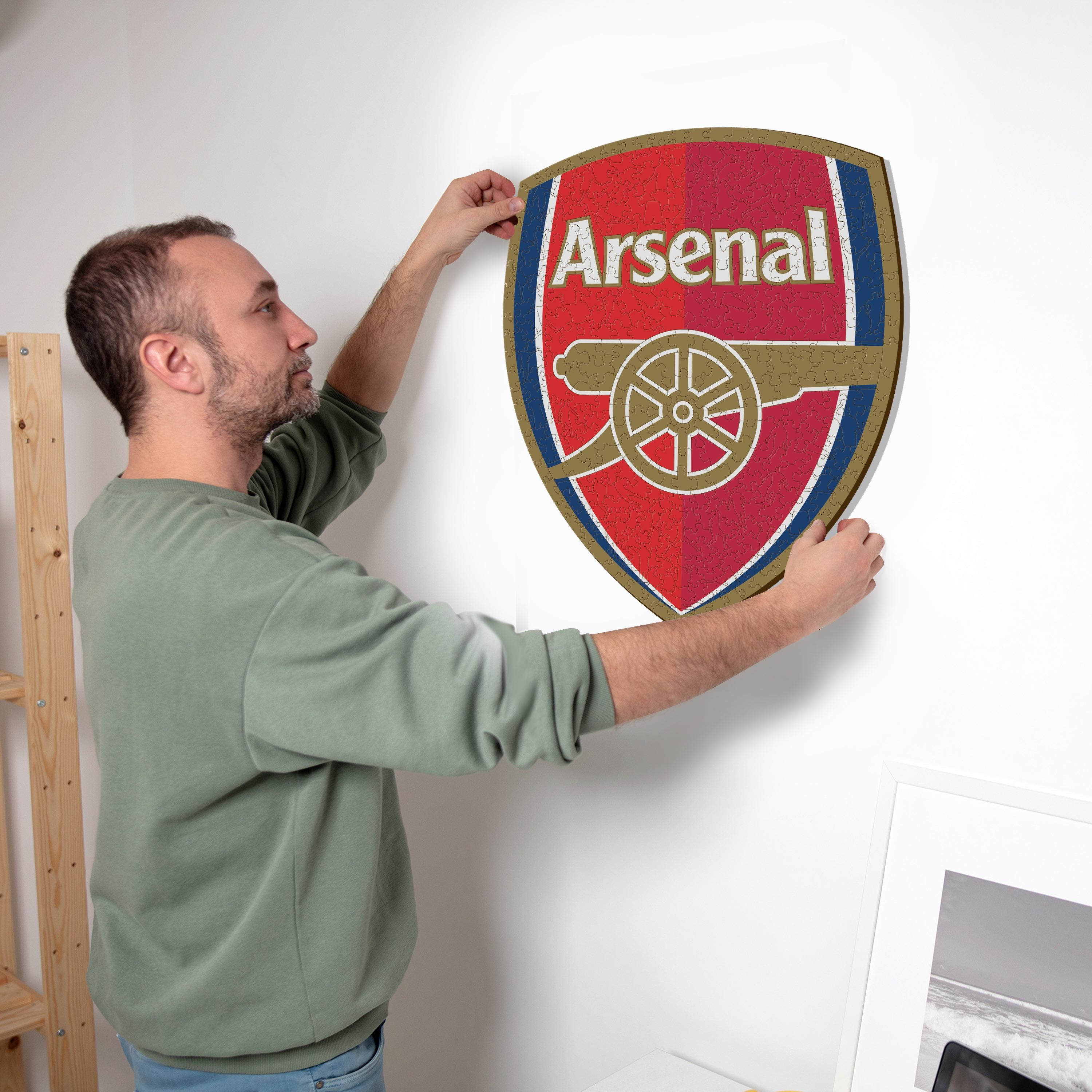 Mann hängt Arsenal-Puzzle-Logo an Wand.