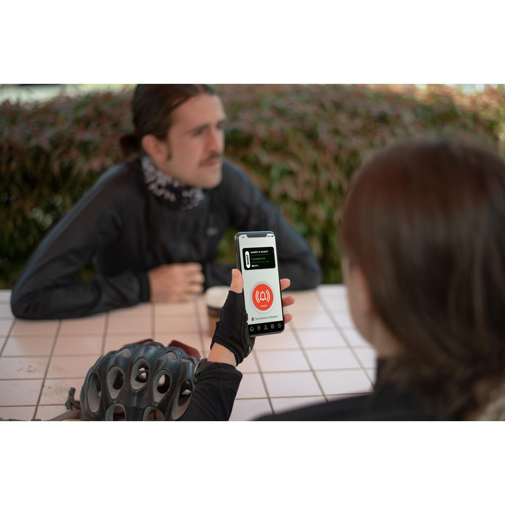 Une personne tient un smartphone affichant une app de notification. Un homme assis au fond.