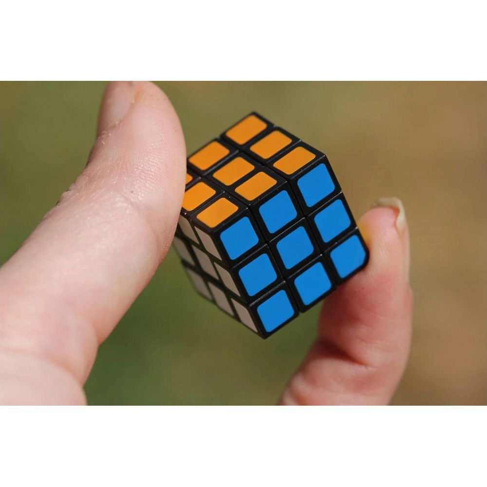 Eine Hand hält einen kleinen, bunten Würfel mit blauen und orangen Seiten.