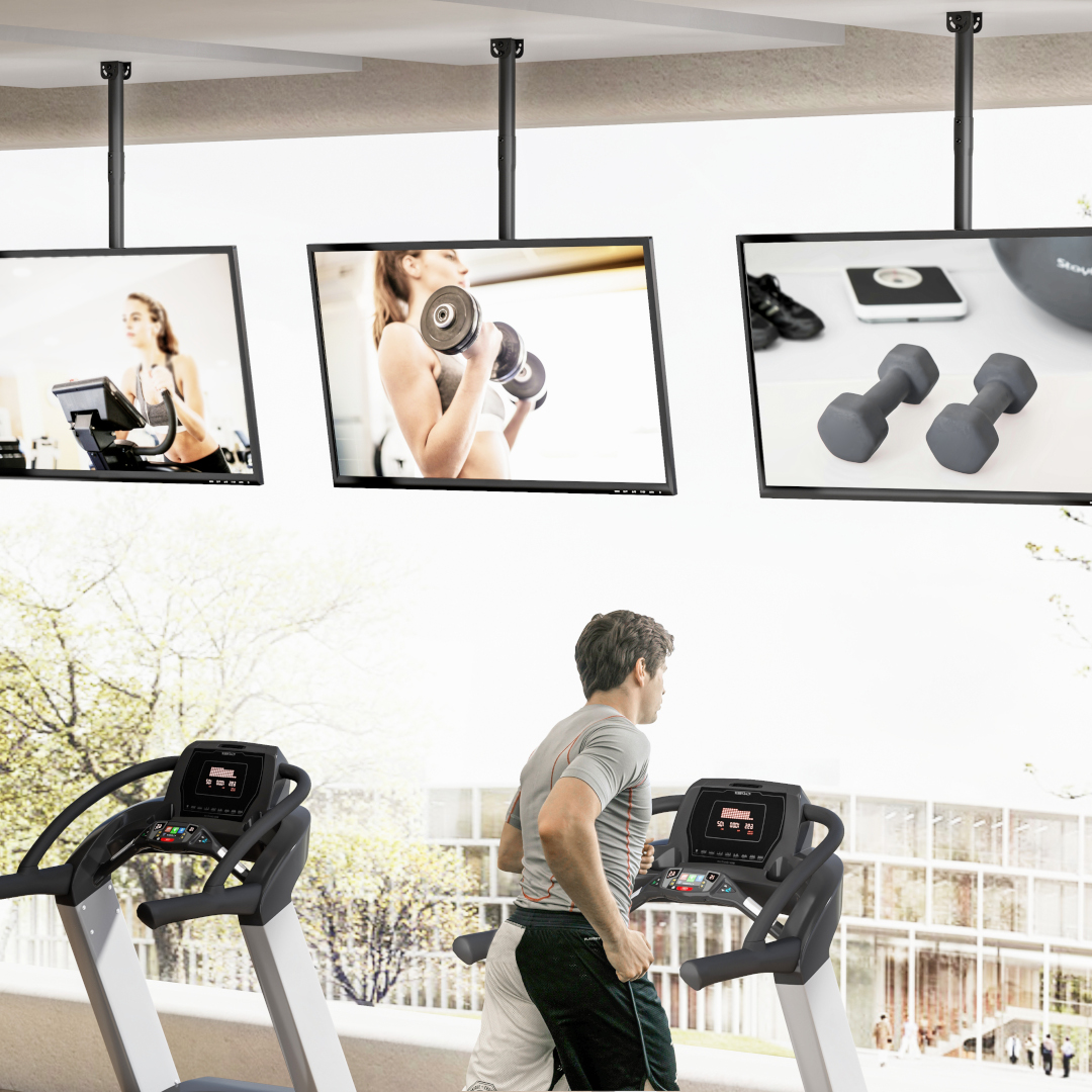 Mann auf Laufband, Frauen auf Bildschirmen im Fitnessstudio, Hanteln.