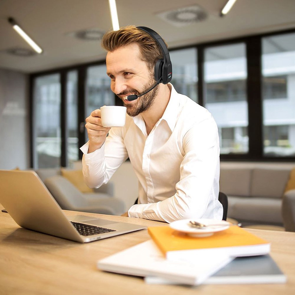 Mężczyzna w słuchawkach pije kawę, patrząc na laptopa.