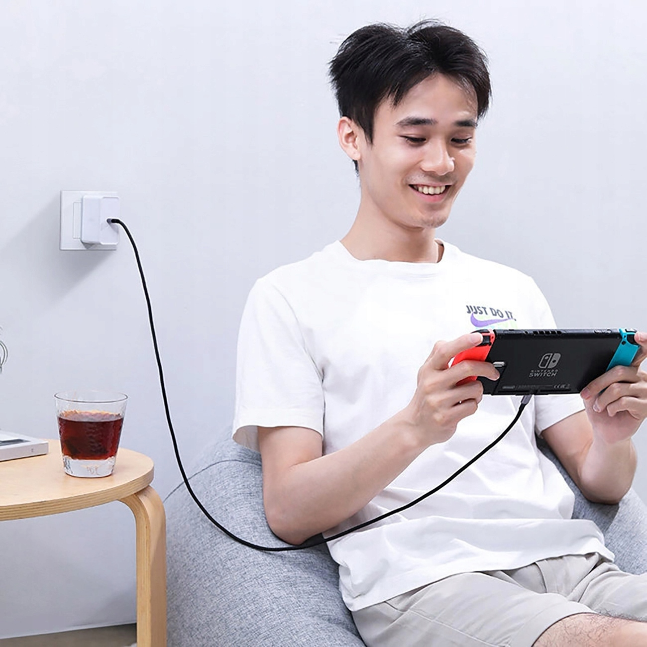 Mężczyzna siedzi, grając w Nintendo Switch. Obok stoi szklanka z ciemnym płynem.