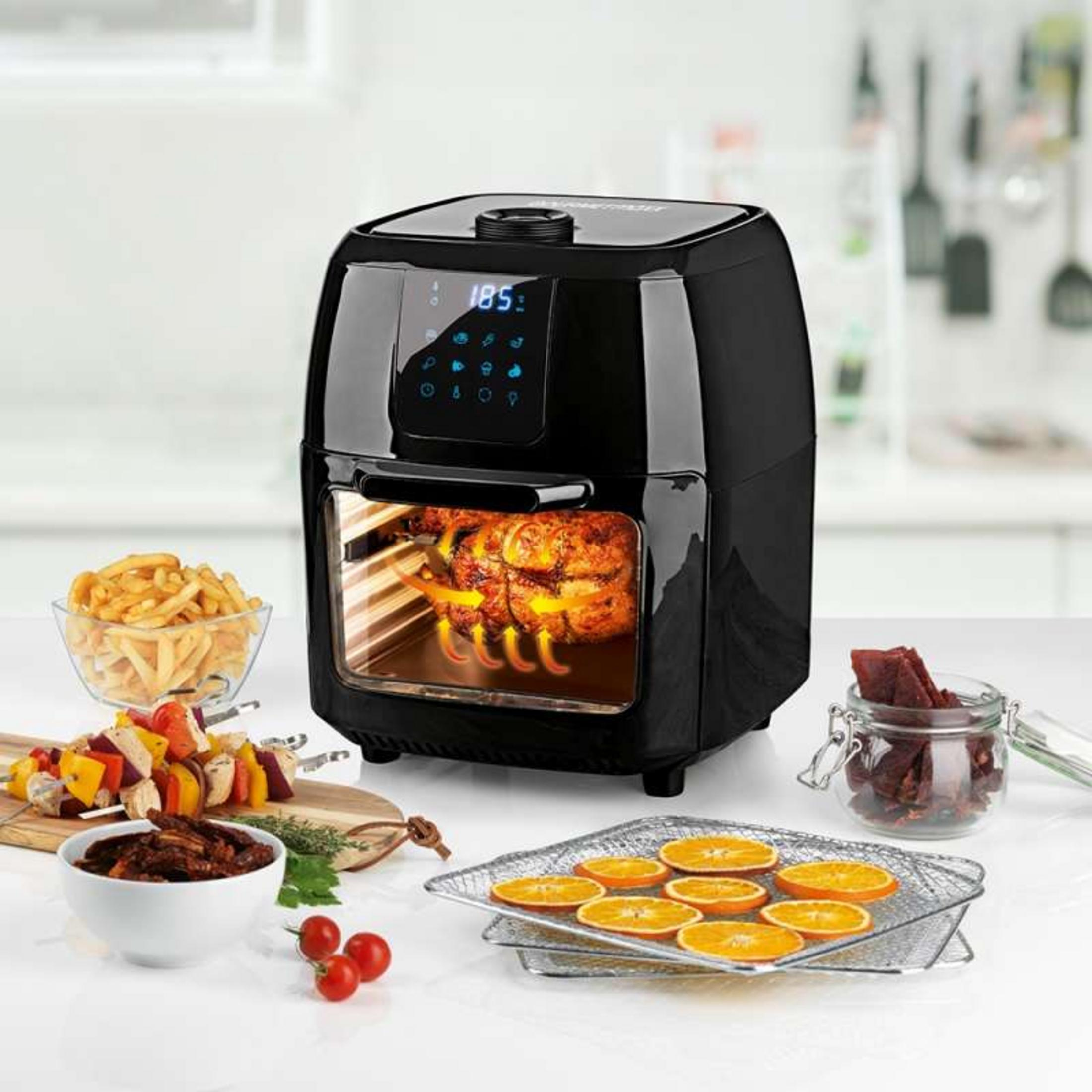 Una friggitrice ad aria nera con un pollo arrosto all'interno. Patatine fritte, spiedini e fette d'arancia sono vicini.