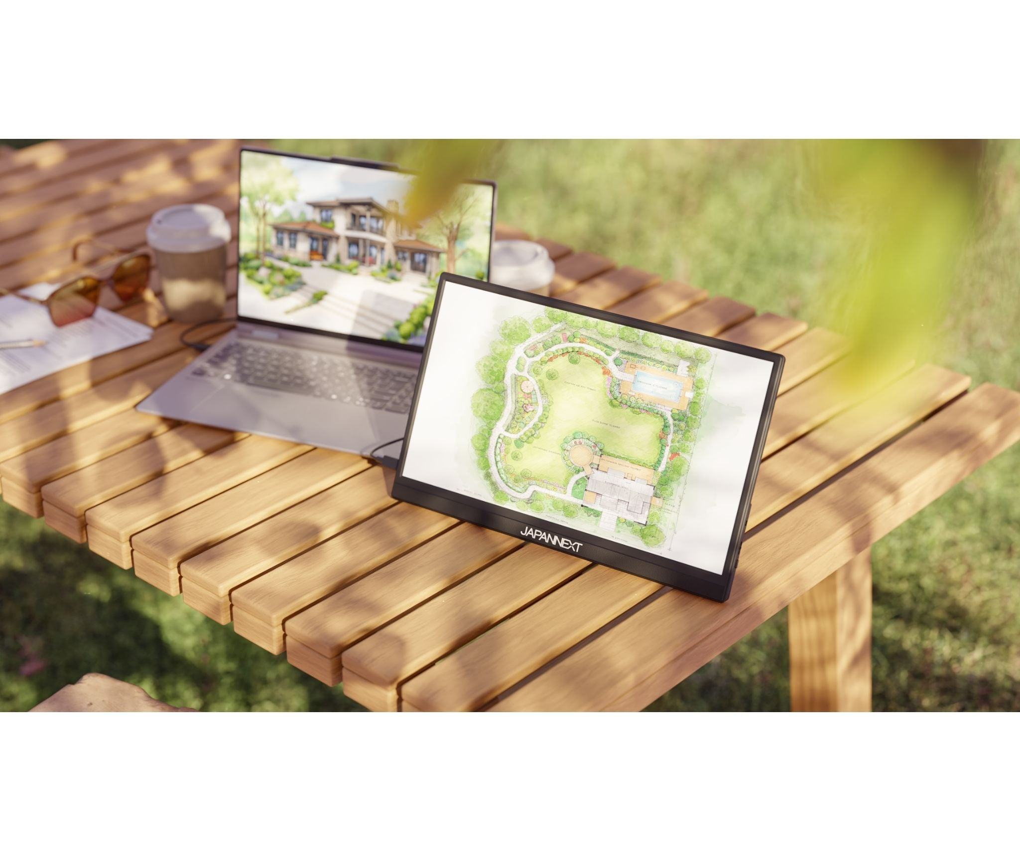 Laptop zeigt Haus, daneben ein Monitor mit Gartenplan. Kaffeetasse und Brille auf Holztisch.