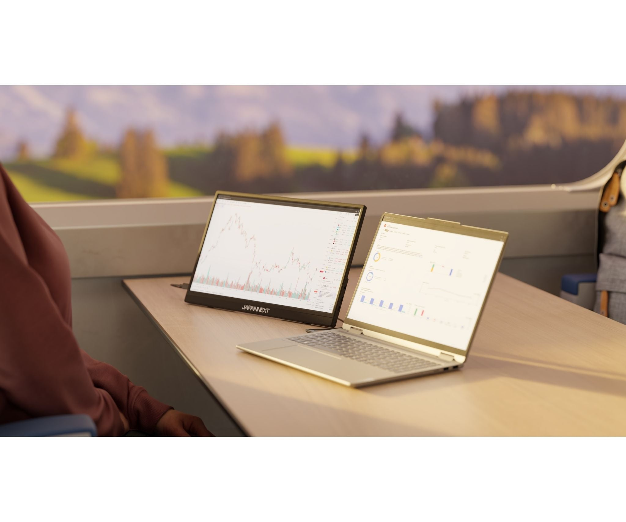 Eine Person sitzt in einem Zug und arbeitet an zwei Laptops mit Diagrammen.