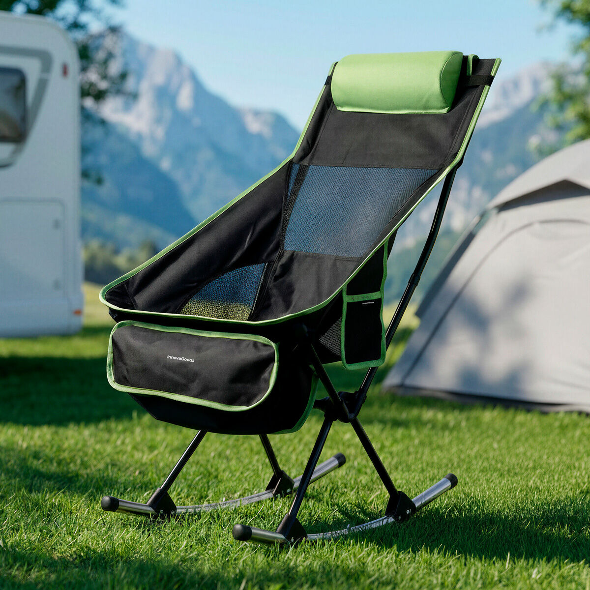 Ein grüner und schwarzer Campingstuhl steht auf Gras, mit Wohnmobil und Zelt im Hintergrund.