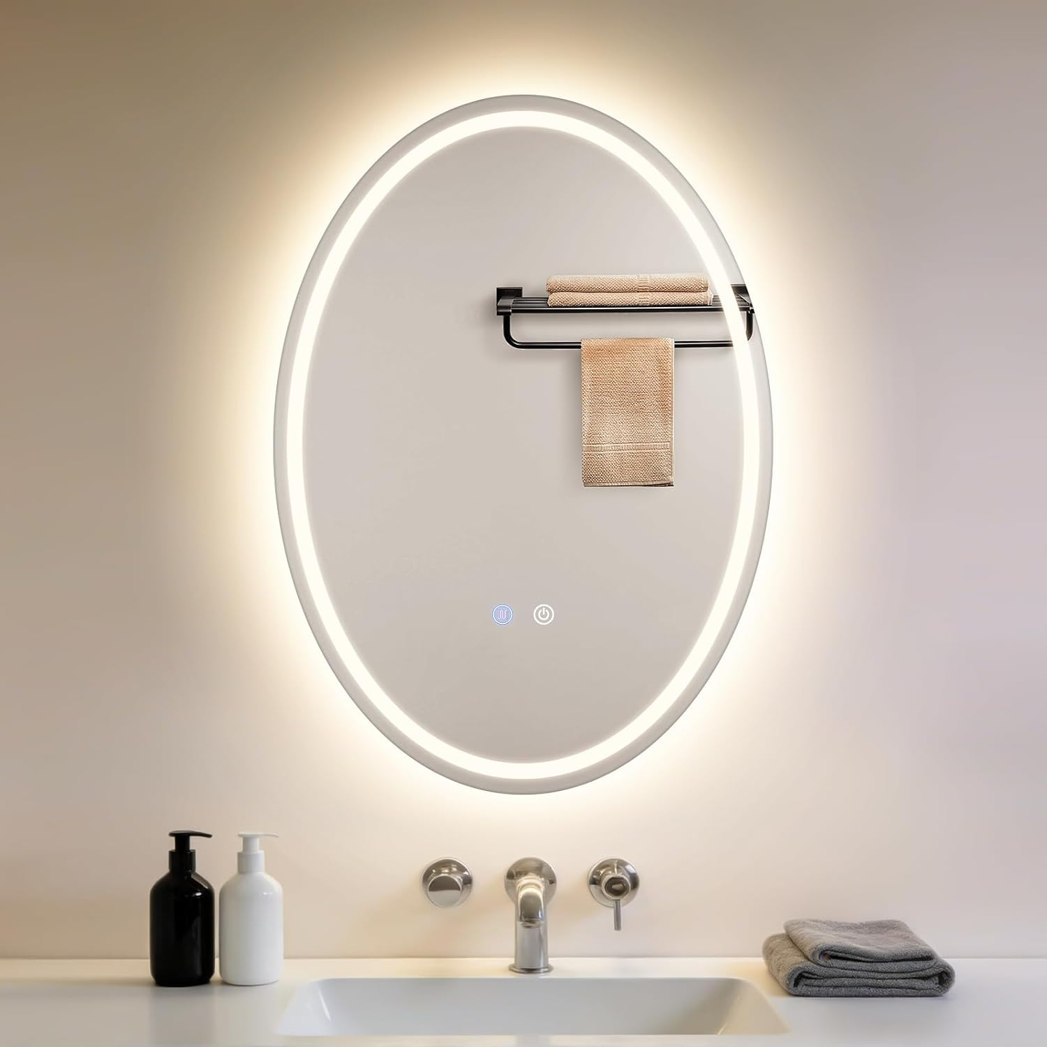 Specchio ovale illuminato sopra il lavandino con dispenser di sapone bianco e nero e asciugamani piegati.