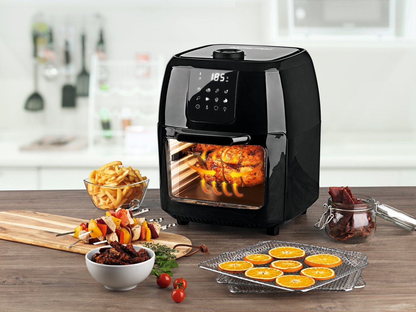 Una friggitrice ad aria nera con un pollo arrosto all'interno, circondata da cibo.