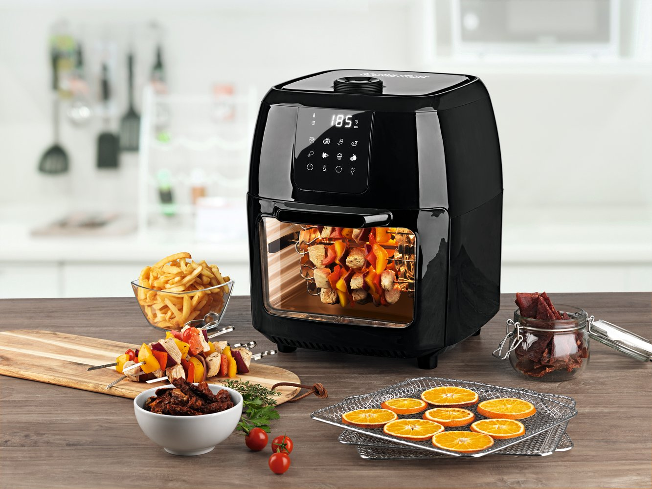 Un forno friggitrice ad aria nero con spiedini di carne, patatine e fette d'arancia.