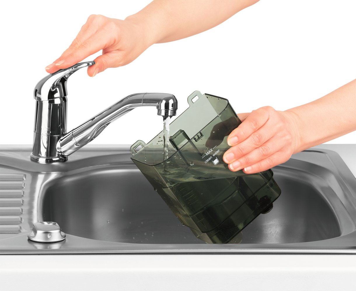 Mani risciacquano un contenitore trasparente sotto acqua corrente in un lavello.