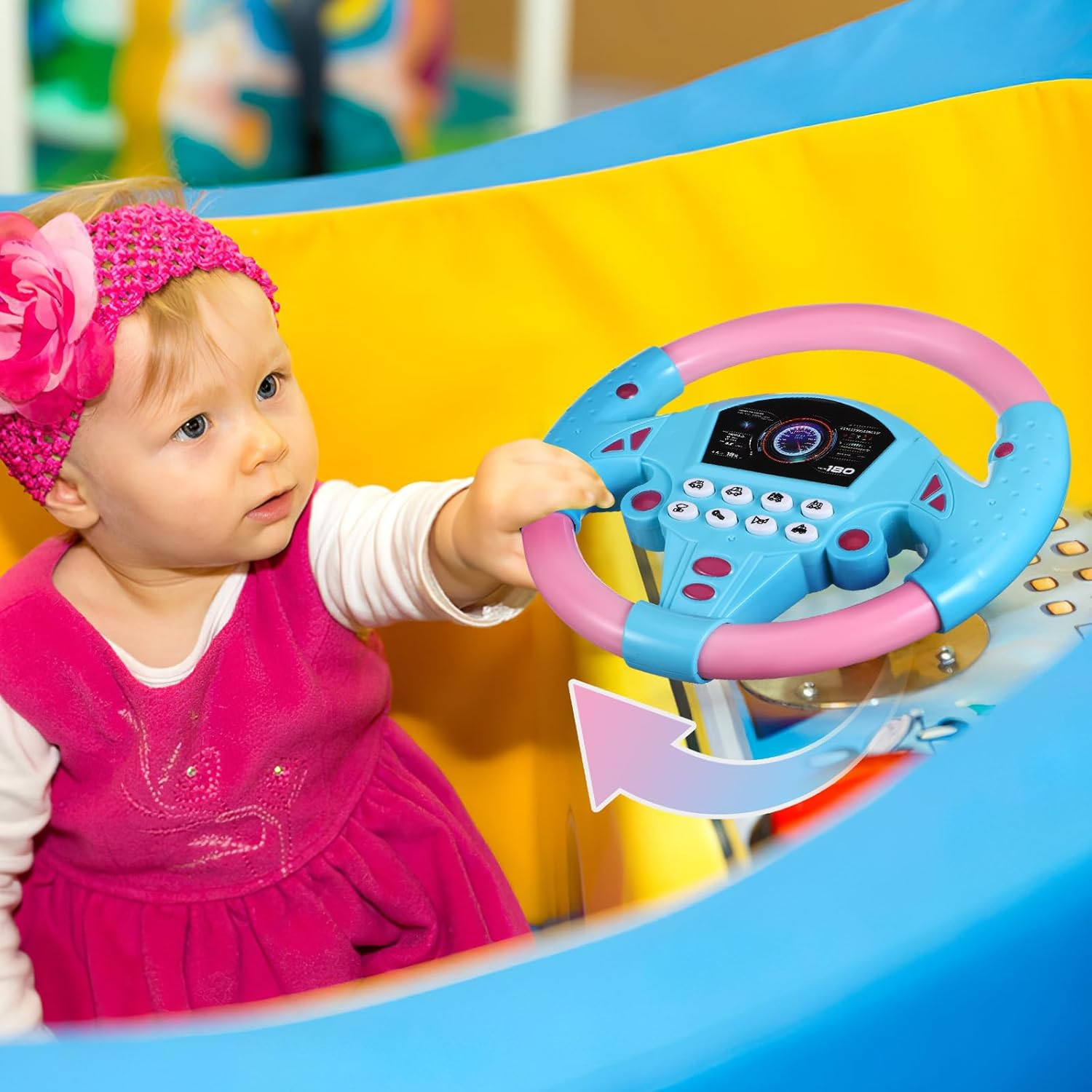 Ein Baby in einem rosa Kleid spielt mit einem blauen und rosa Spielzeuglenkrad.
