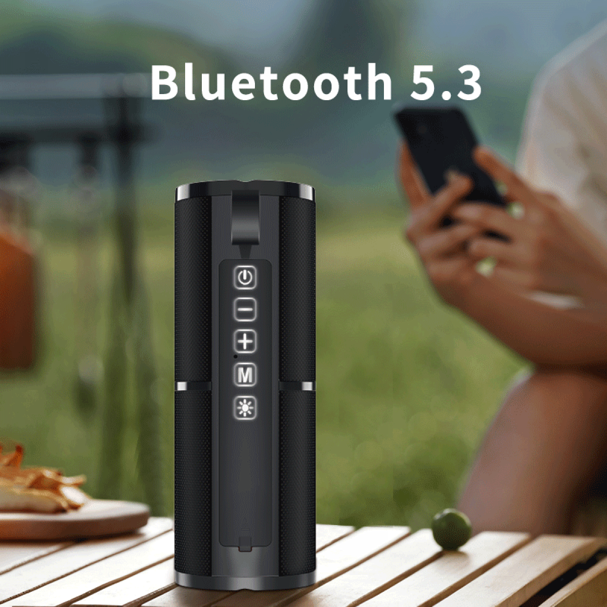 Schwarzer Bluetooth-Lautsprecher mit Bedienelementen auf einem Holztisch im Freien.