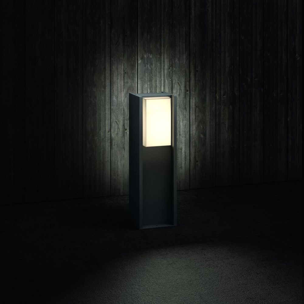 Ciemna lampa słupowa z podświetlanym blatem stoi przed drewnianą ścianą.