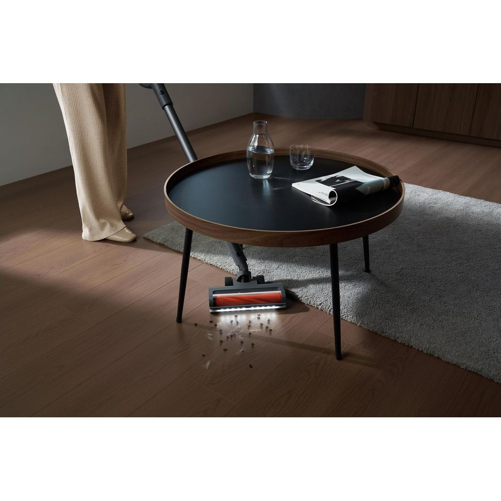 Czyszczenie podłogi: Odkurzacz wciąga zanieczyszczenia przed okrągłym stołem.