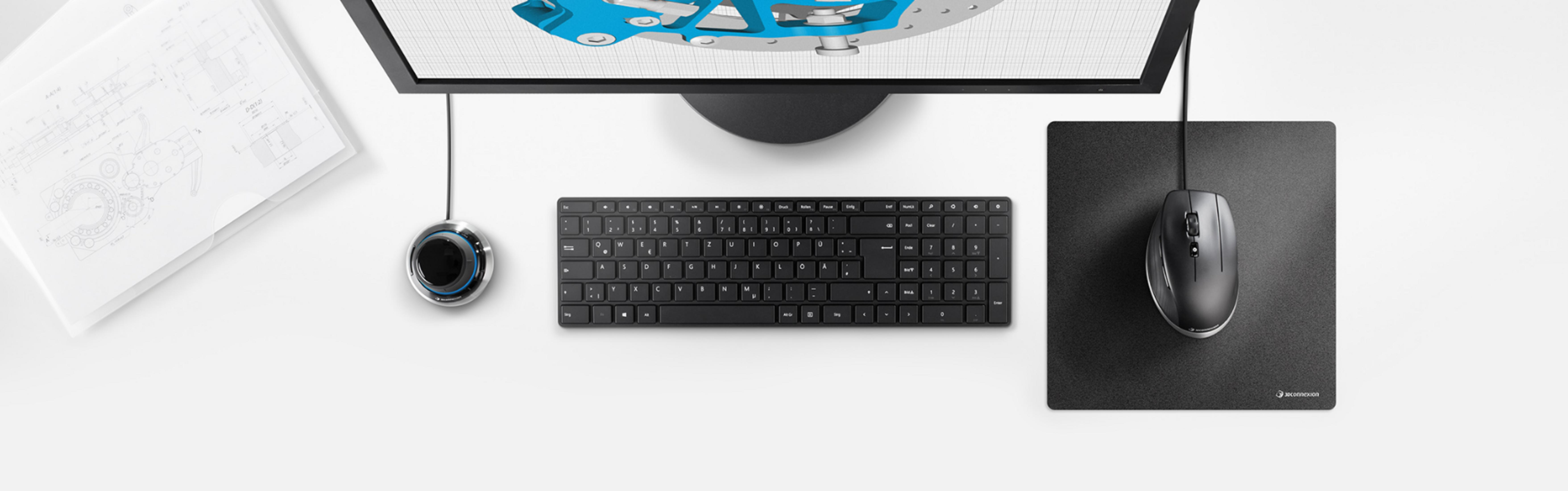 Ein Schreibtisch mit Monitor, Tastatur, Maus, 3D-Maus und technischen Zeichnungen.