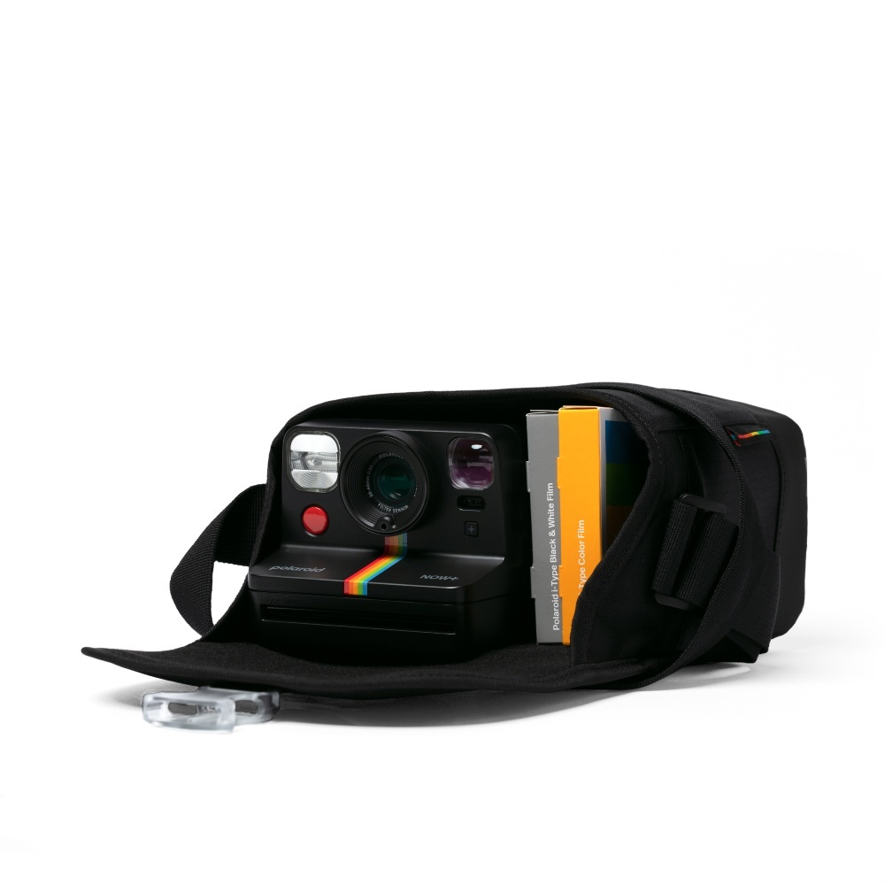 Fotocamera Polaroid nera con striscia arcobaleno in borsa con pacchi di pellicole.