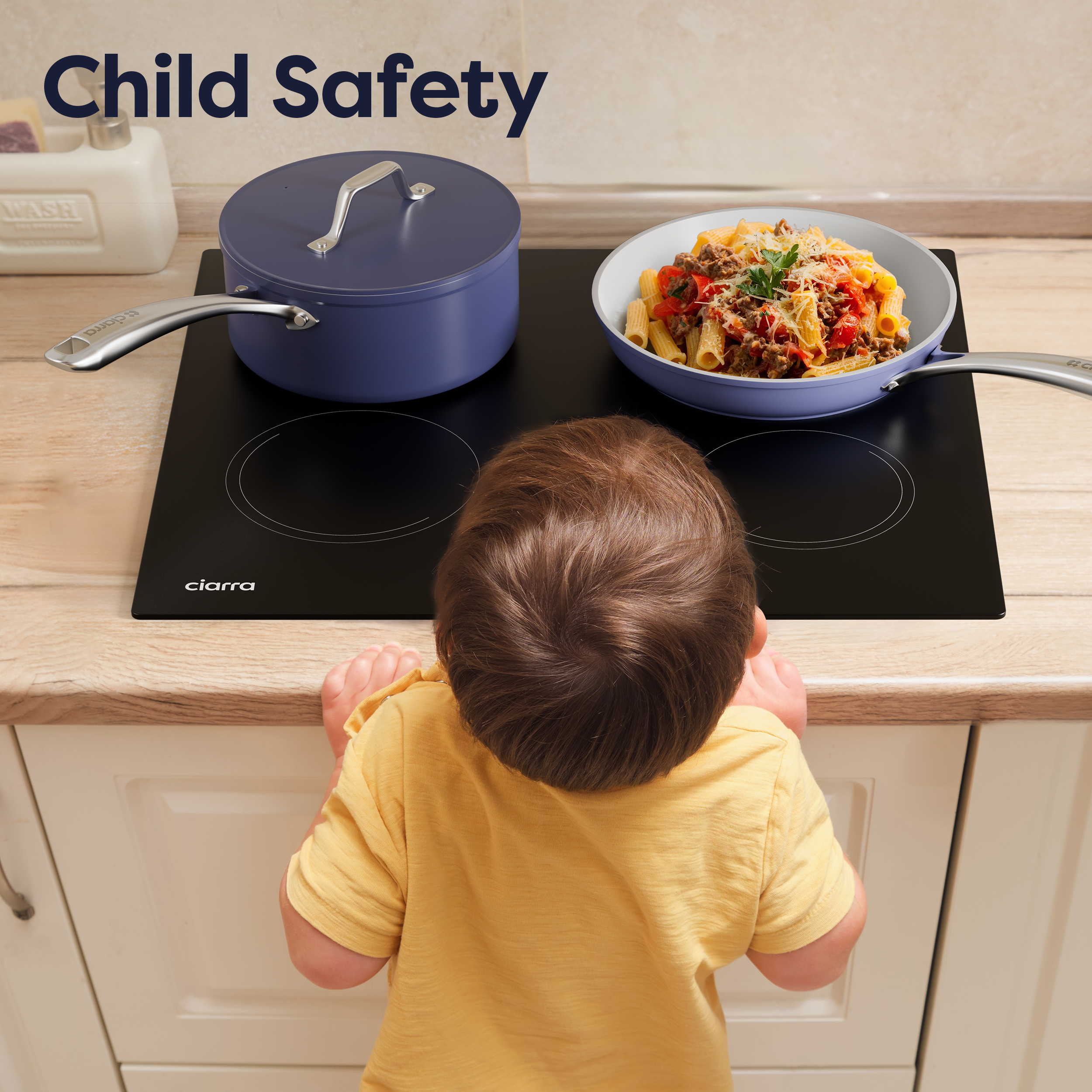 Un enfant en chemise jaune se tient devant une plaque de cuisson avec une casserole et une poêle.