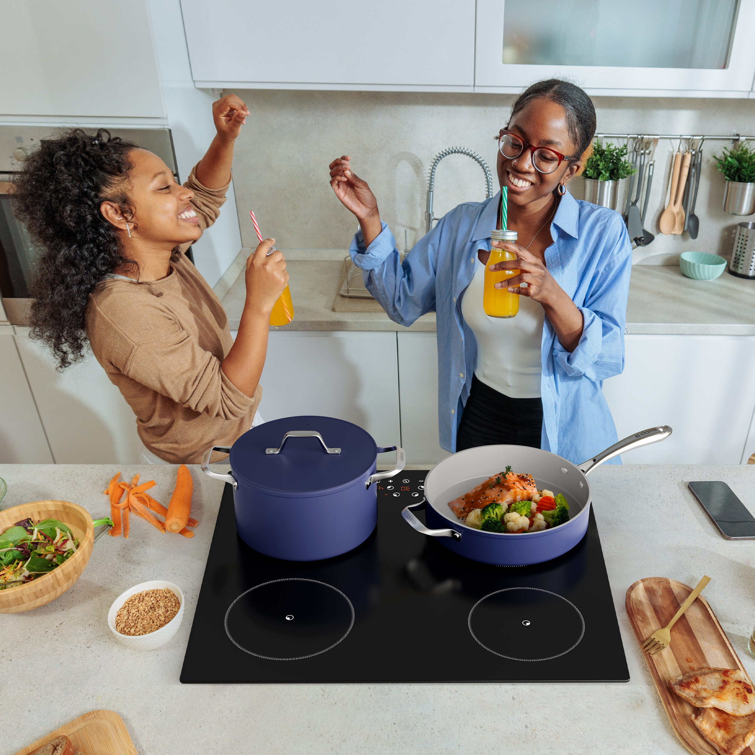 Deux femmes dansent dans la cuisine en buvant du jus. Le poisson cuit.