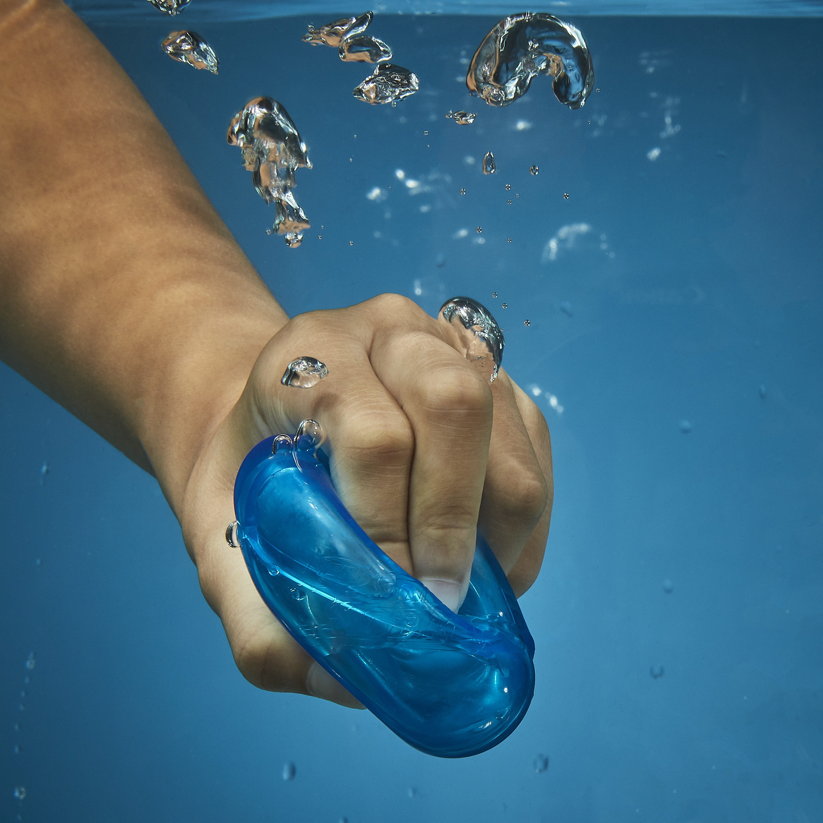 Eine Hand hält eine blaue Schwimmbrille unter Wasser. Blasen steigen auf.