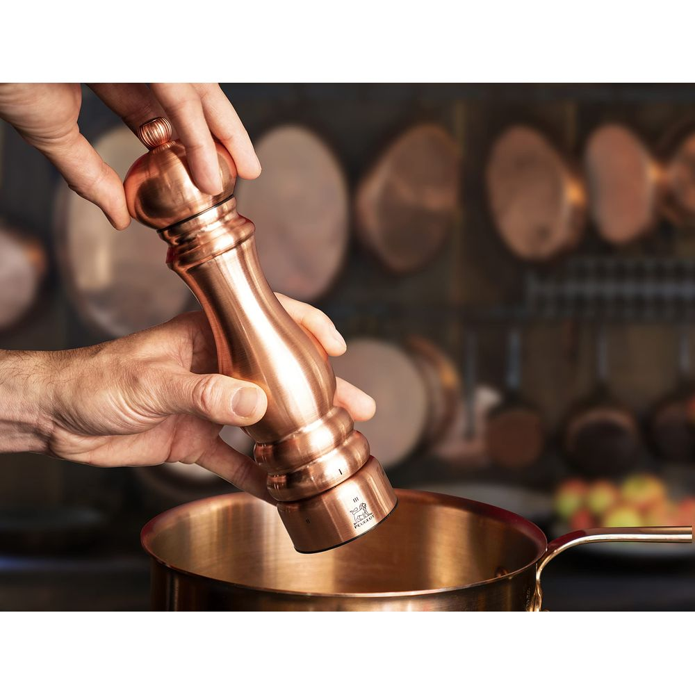 Eine kupferfarbene Pfeffermühle wird über einem Kupfertopf gehalten.