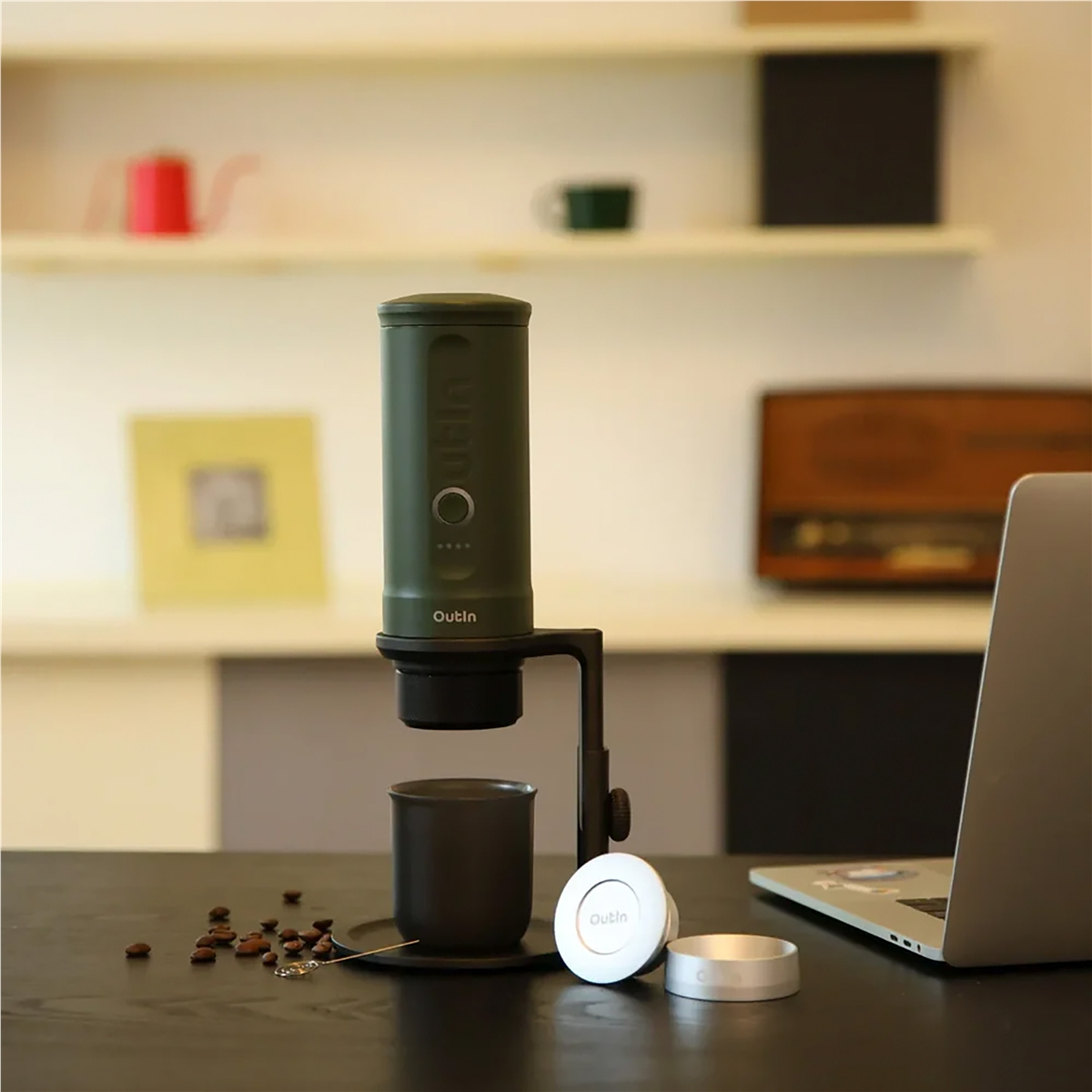Cafetera verde con taza y granos sobre una mesa.