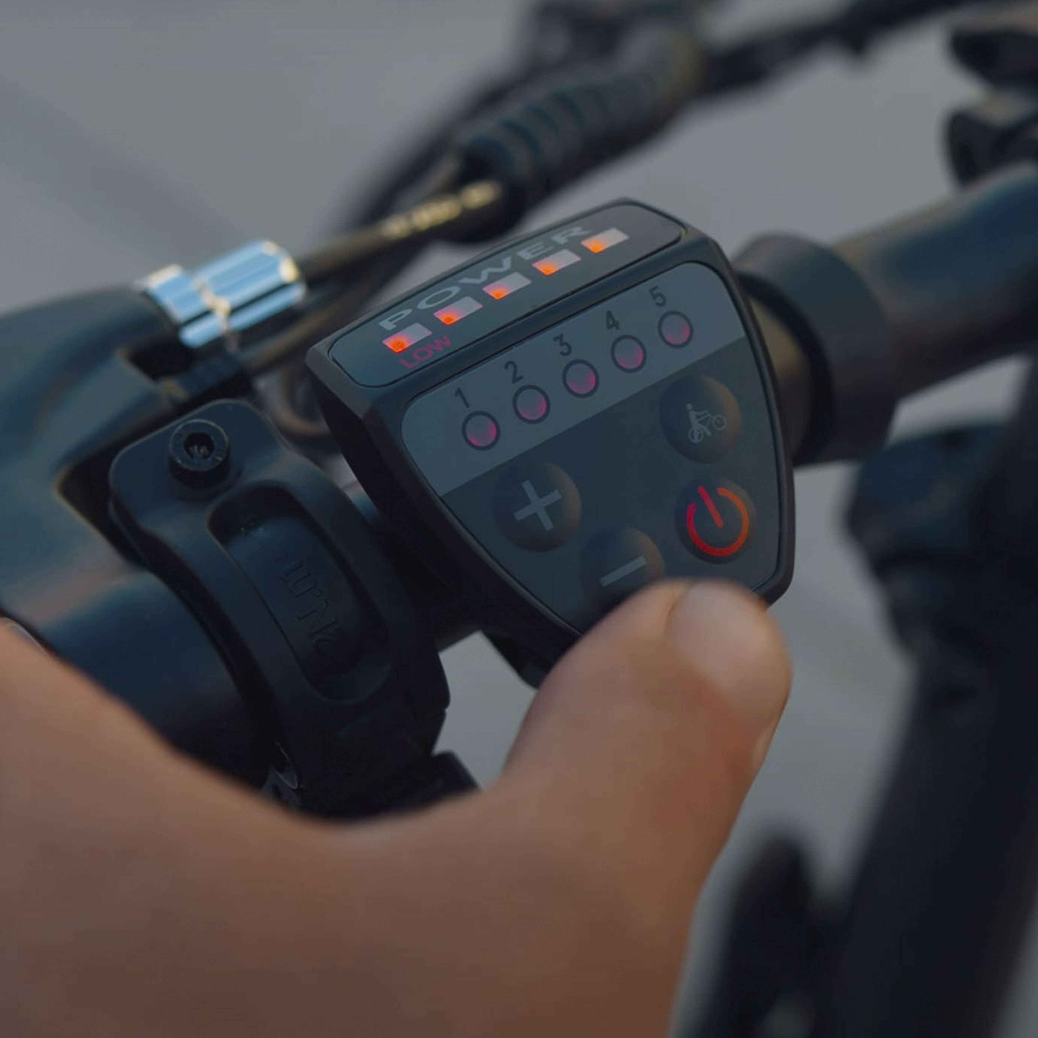 Primer plano de una mano operando una pantalla de bicicleta eléctrica con luces rojas encendidas.