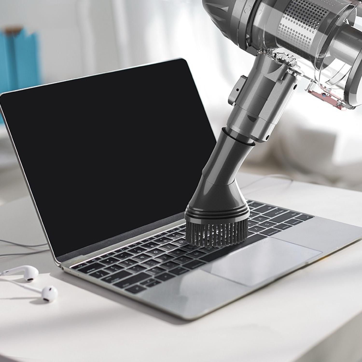 Ein Staubsauger reinigt die Tastatur eines Laptops.