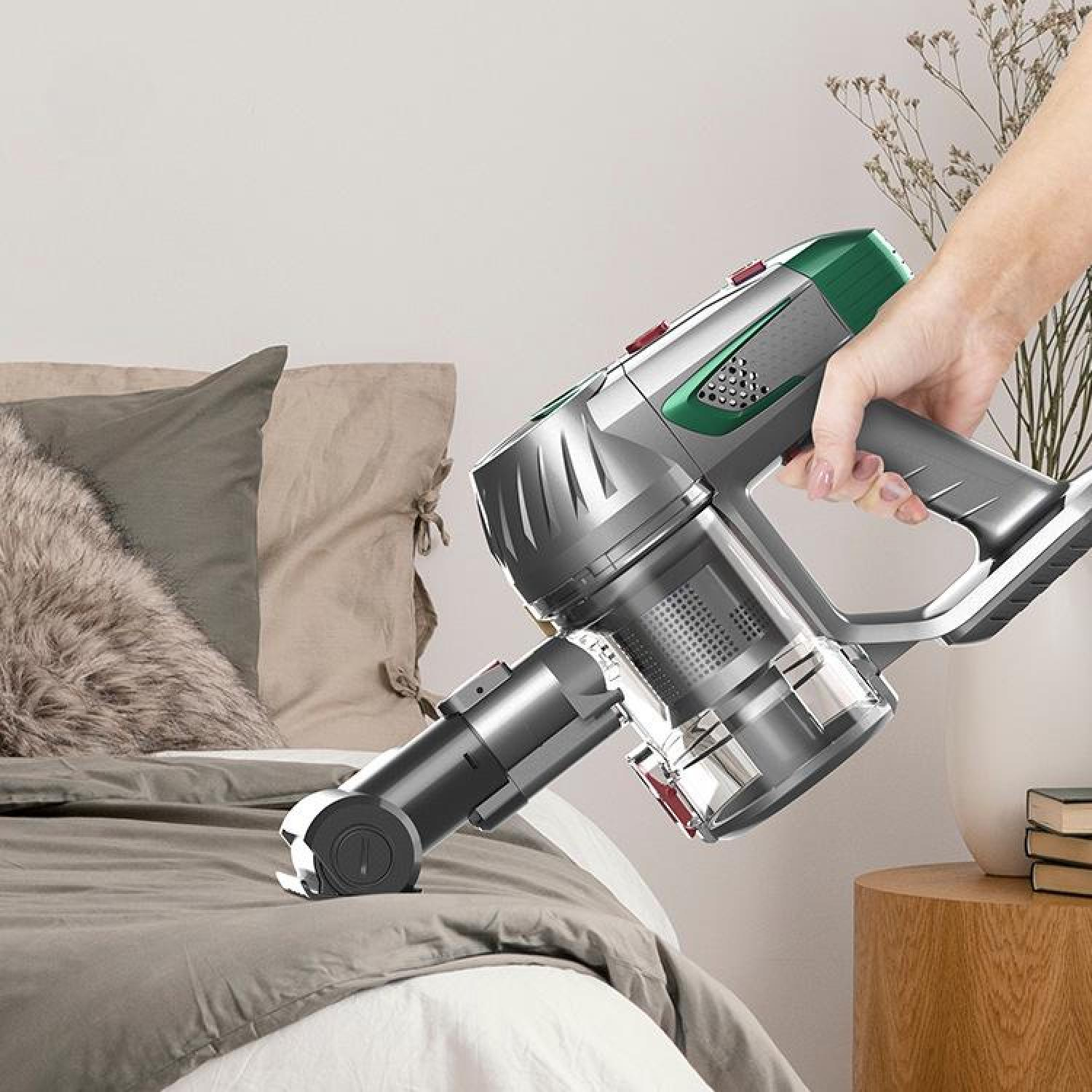 Eine Hand hält einen Akku-Staubsauger über einem Bett zum Reinigen.
