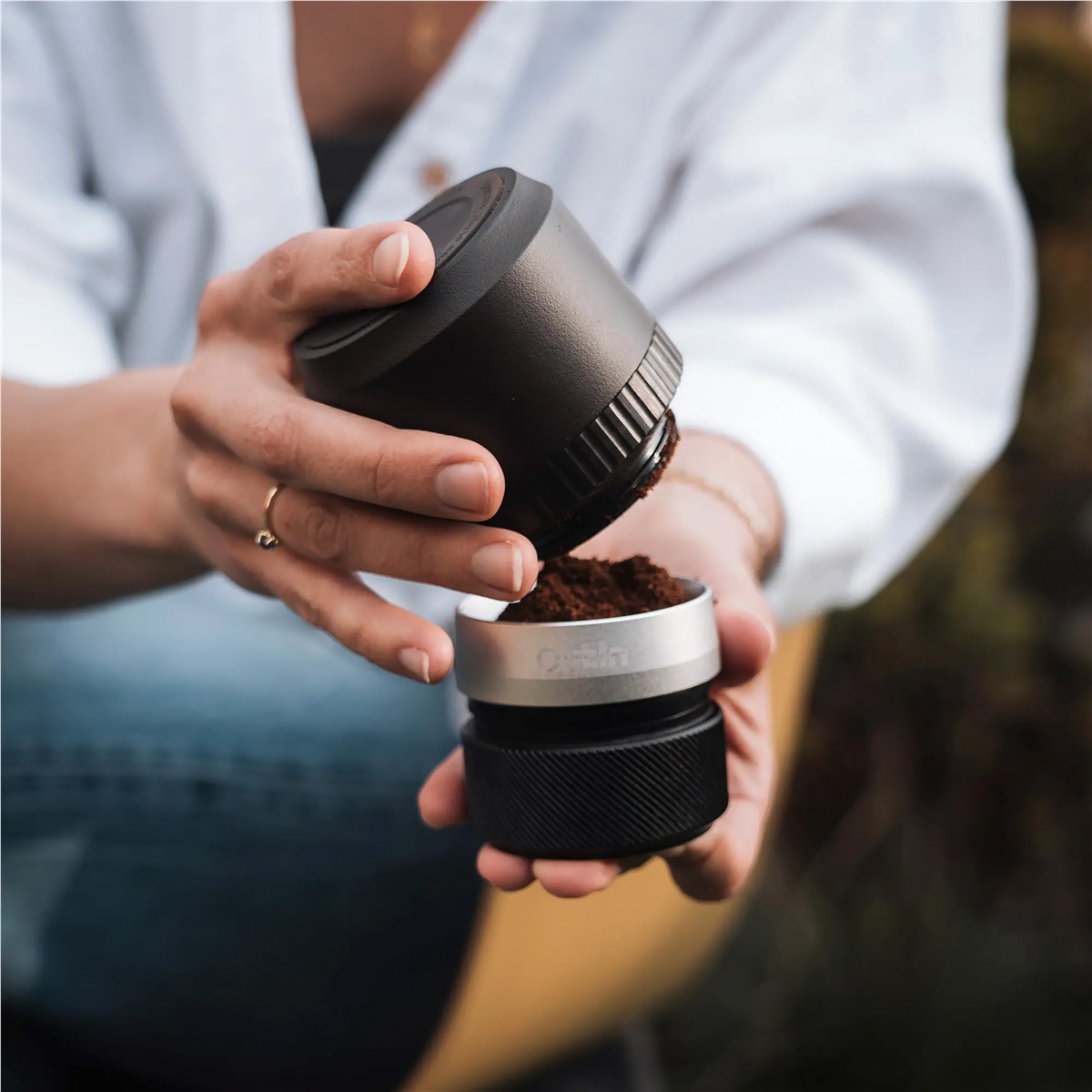 Una persona vierte café molido de un contenedor negro en un contenedor plateado.