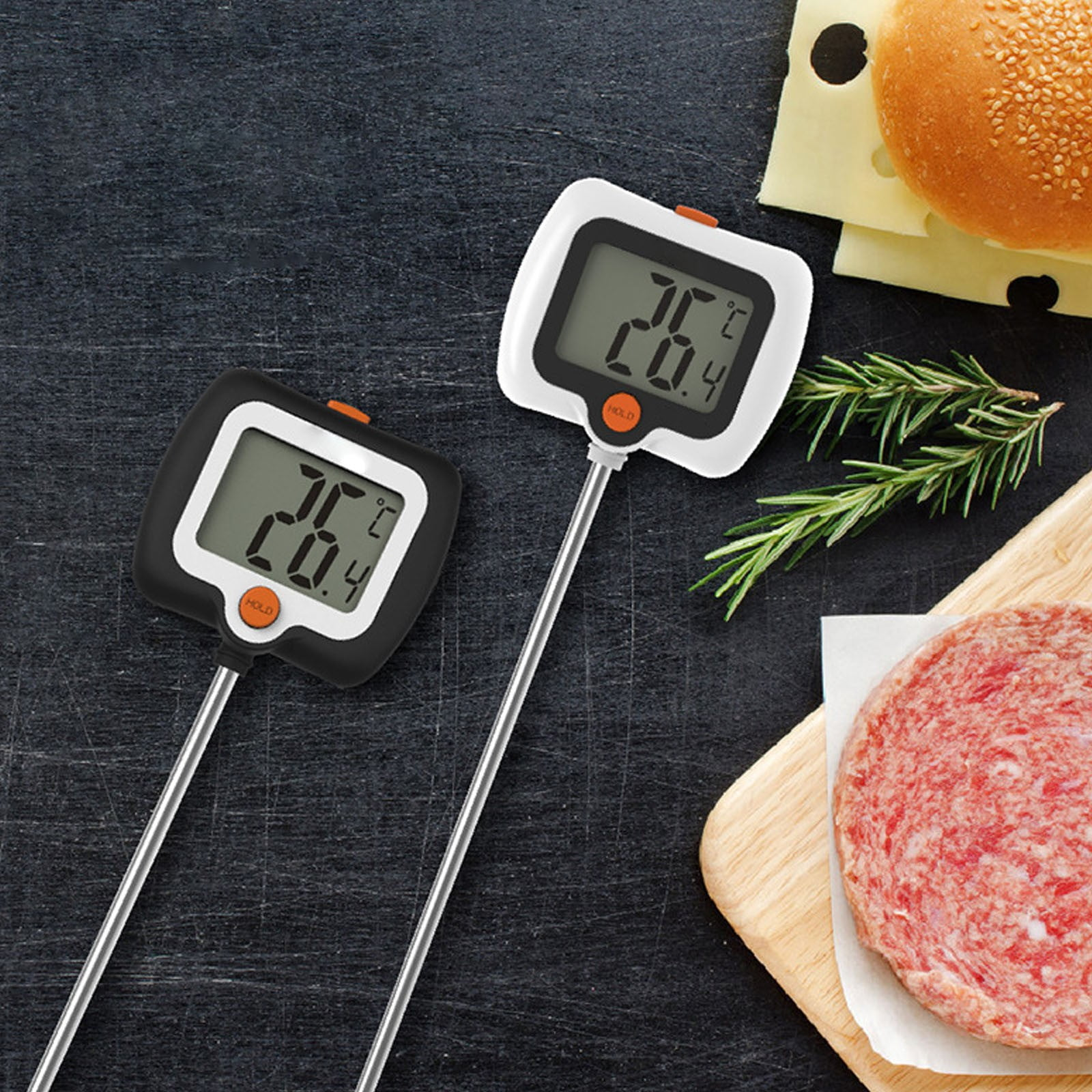 Zwei digitale Fleischthermometer liegen auf einer dunklen Oberfläche neben Essen.
