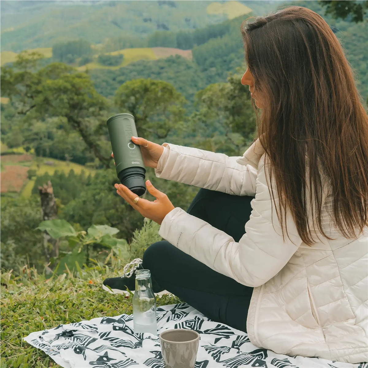 Mujer sosteniendo contenedor verde al aire libre con paisaje montañoso.