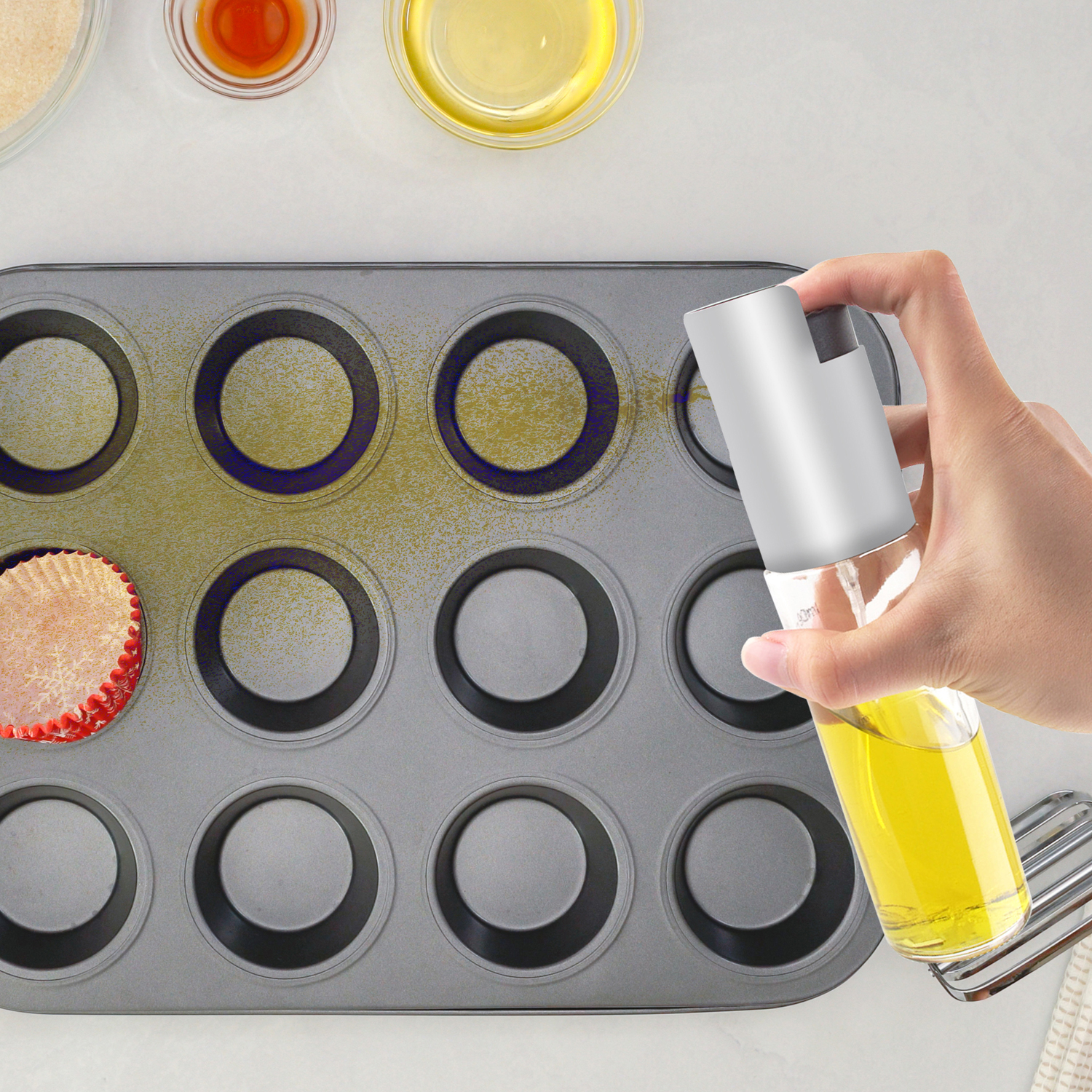 Uno spruzzino d'olio viene usato per ungere uno stampo per muffin.