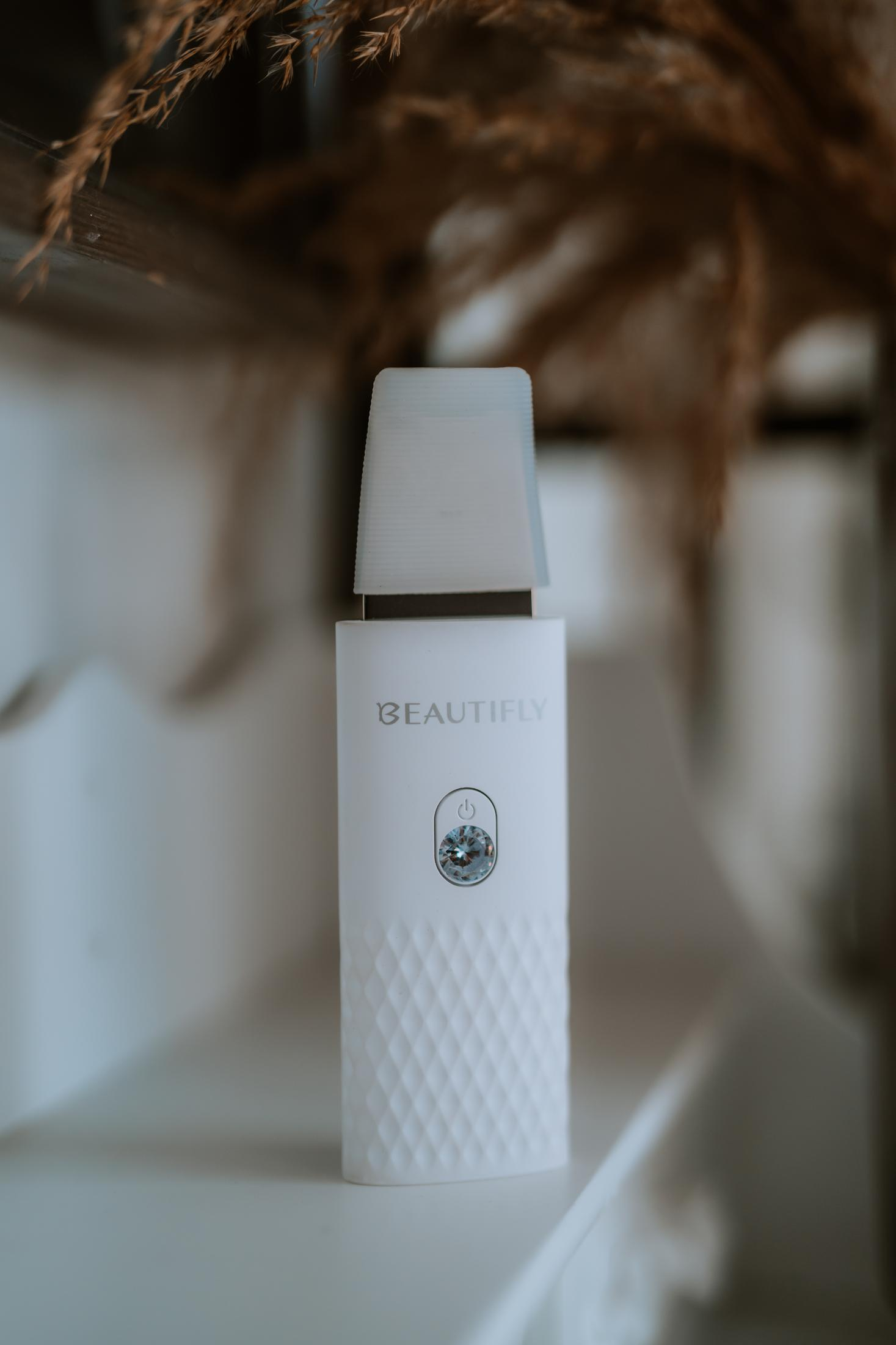 Białe urządzenie Beautify z fasetowanym kamieniem i symbolem zasilania.