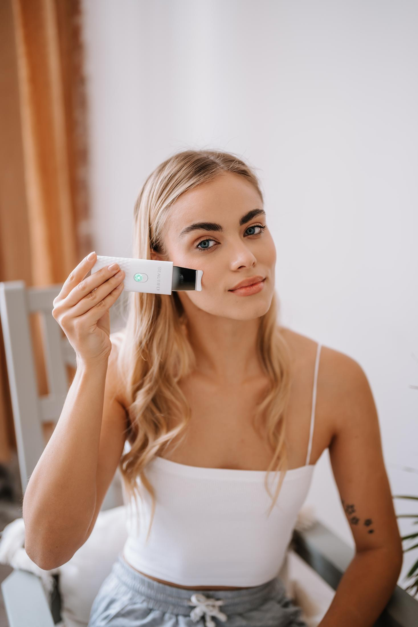 Blondynka używa urządzenia do pielęgnacji twarzy.