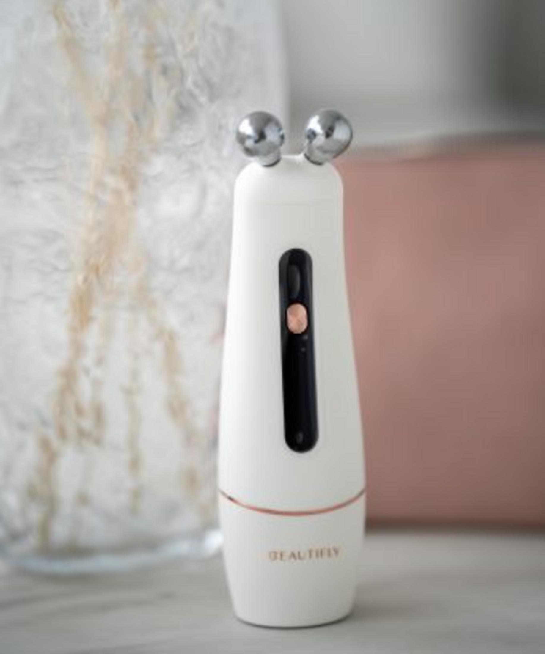 Białe urządzenie do pielęgnacji skóry z dwiema metalowymi kulkami na górze i czarnym ekranem.