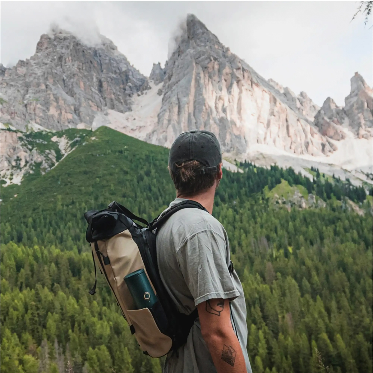Mann mit Rucksack blickt auf neblige Berge und dichten grünen Wald.