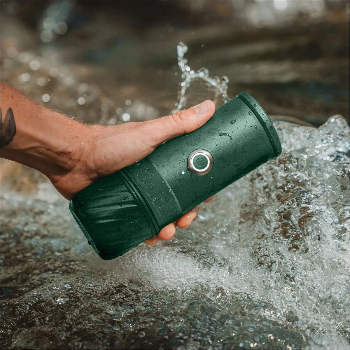 Dunkelgrüner Behälter in Hand über fließendem Wasser mit Spritzern.