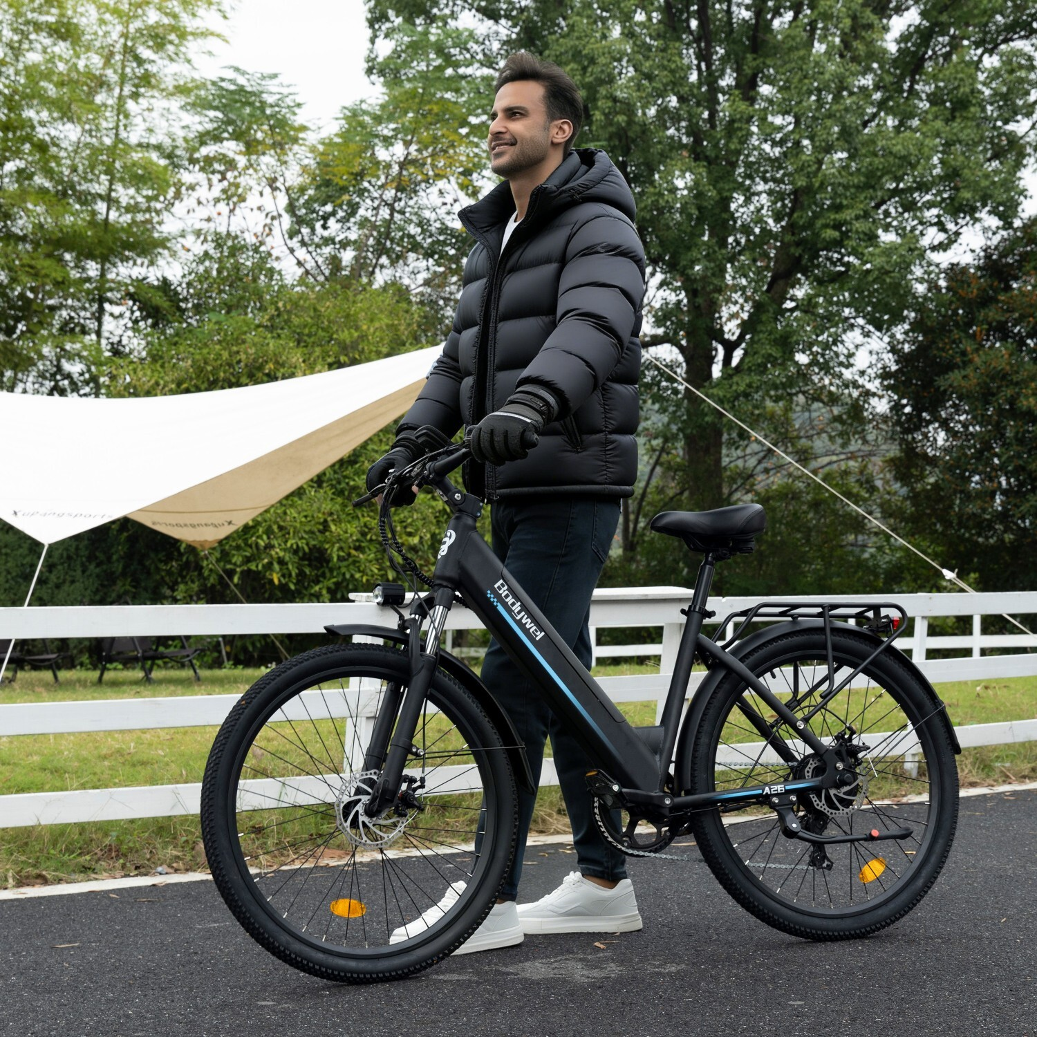 Mężczyzna w czarnej kurtce puchowej obok czarnego roweru elektrycznego na asfalcie.