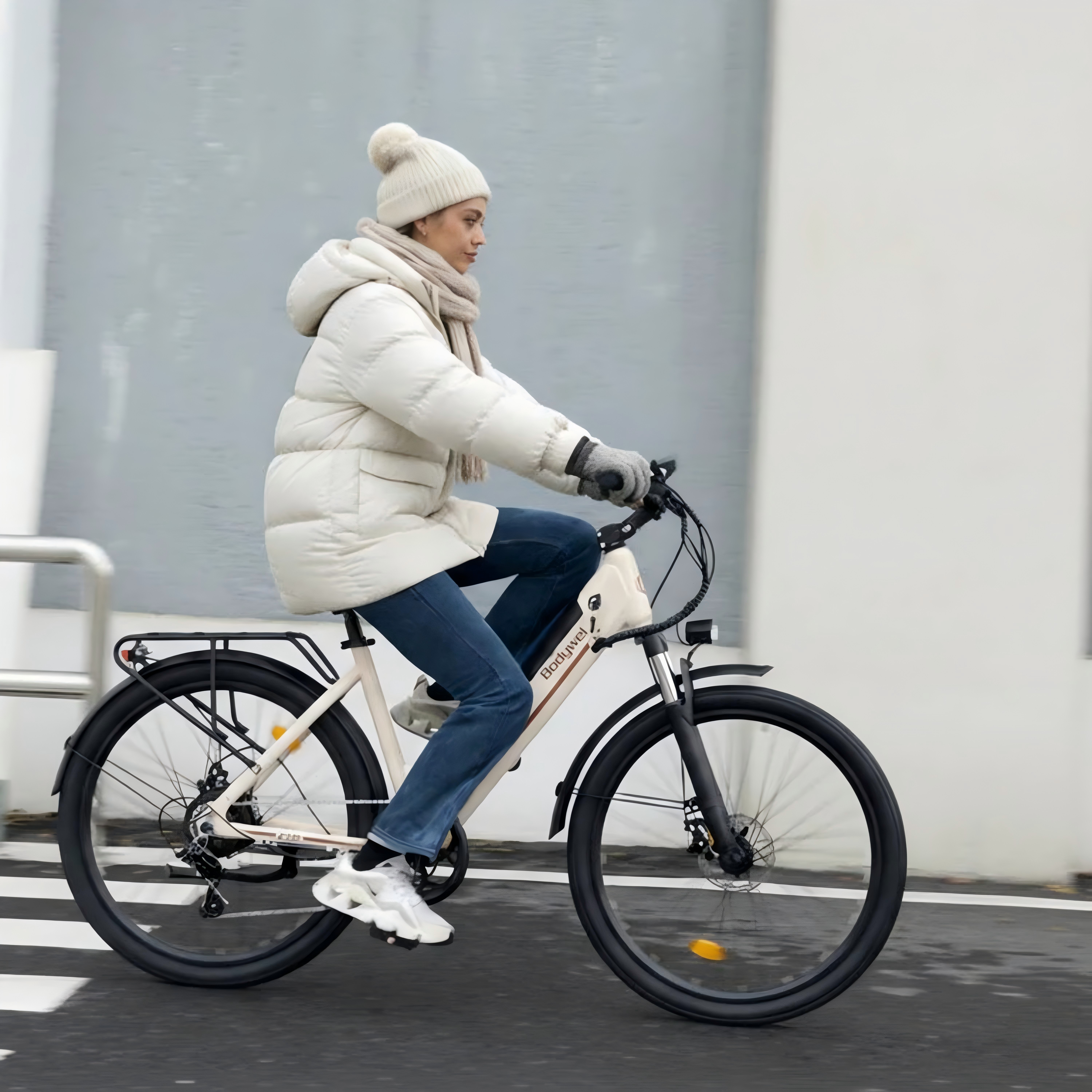 Kobieta w zimowym ubraniu jedzie jasnobeżowym rowerem po ulicy.