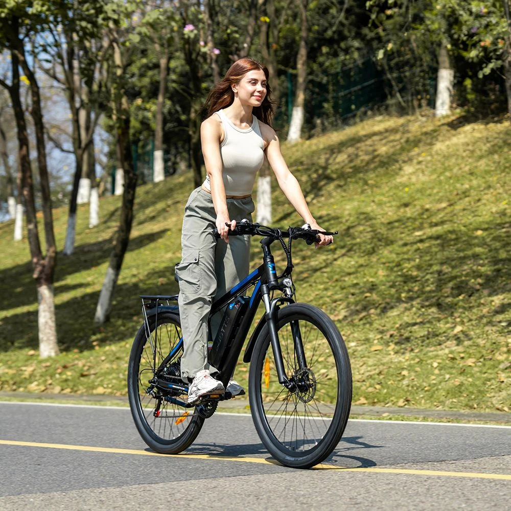 Una donna guida una bicicletta elettrica nera su una strada circondata da alberi.