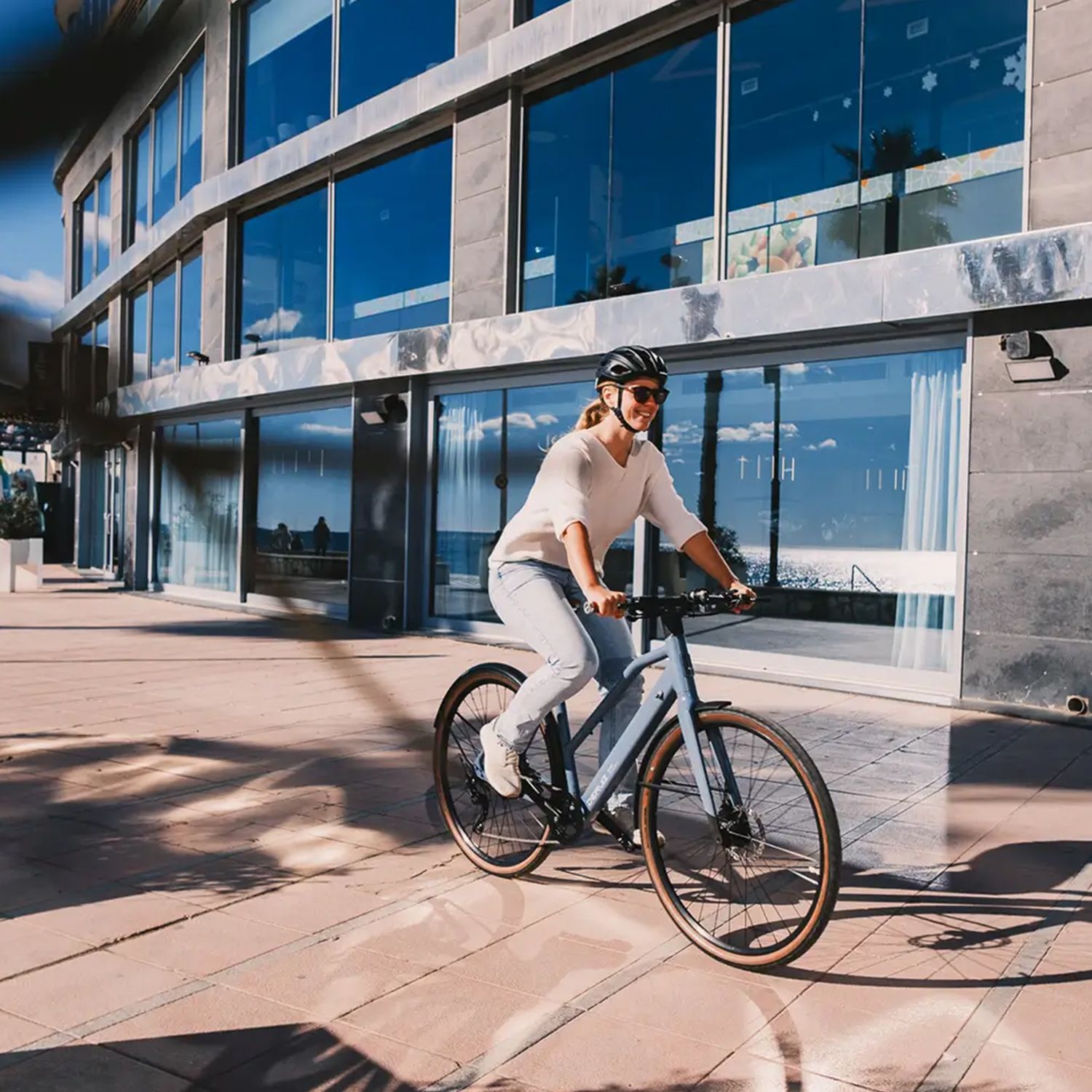 Eine Frau fährt Fahrrad vor einem modernen Gebäude am Wasser.
