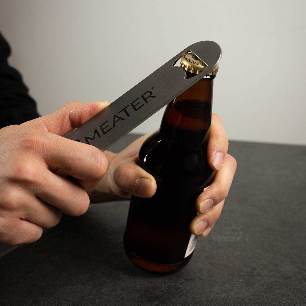 Person öffnet eine Bierflasche mit einem Metall-Flaschenöffner.