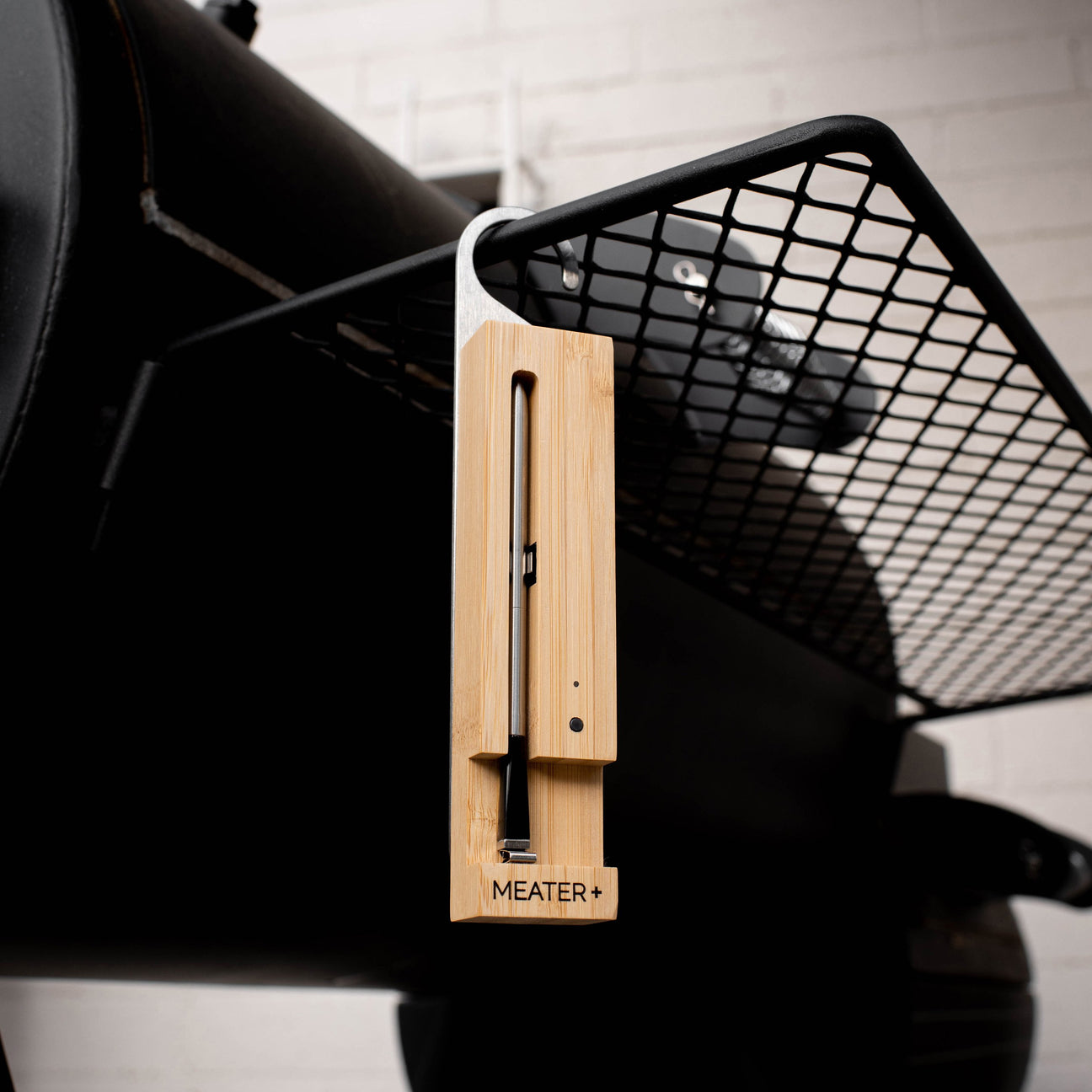 Ein digitaler Fleischthermometer aus Bambus hängt an einem Grillrost.