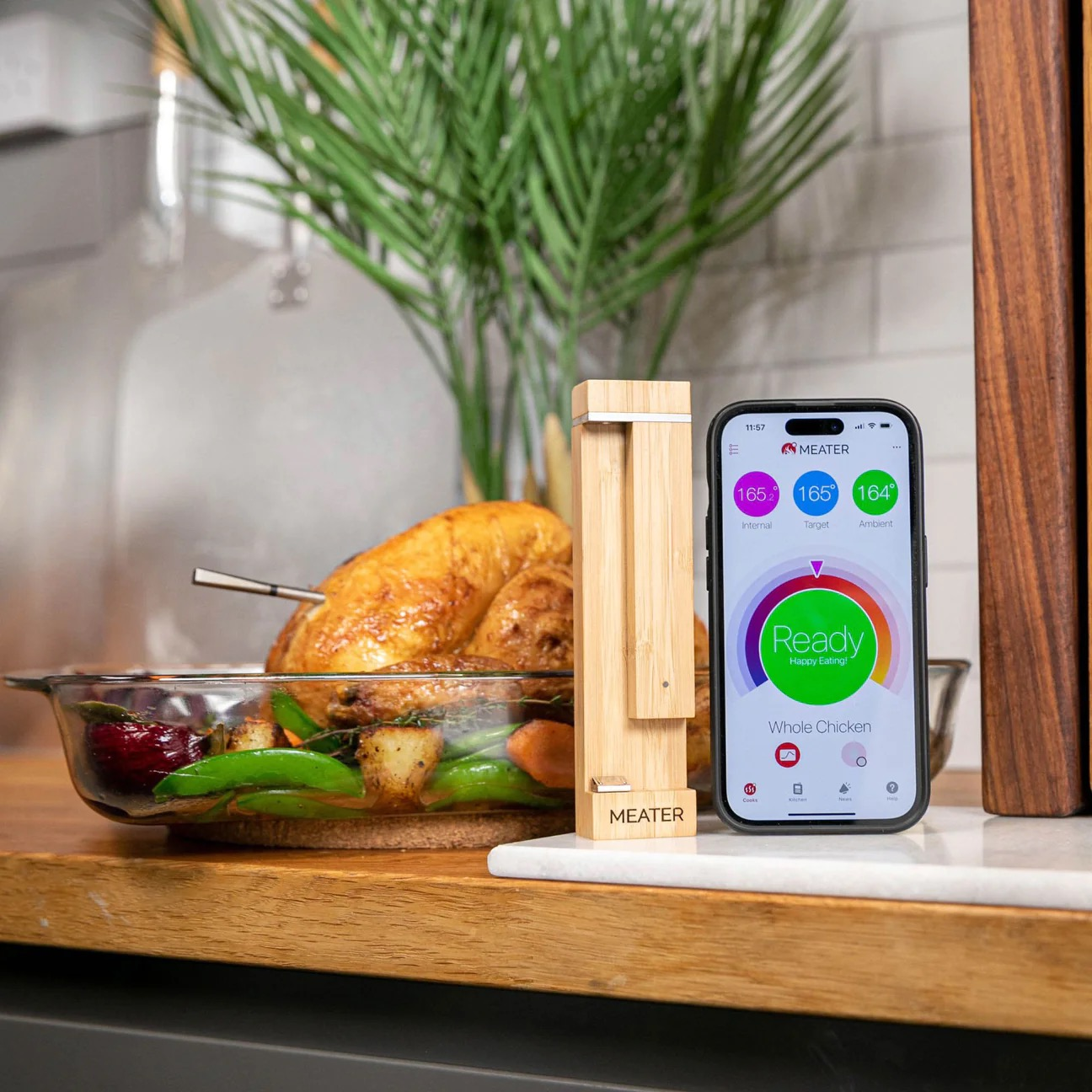 Un poulet rôti dans un plat avec des légumes, à côté d'un thermomètre Meater et d'un smartphone.