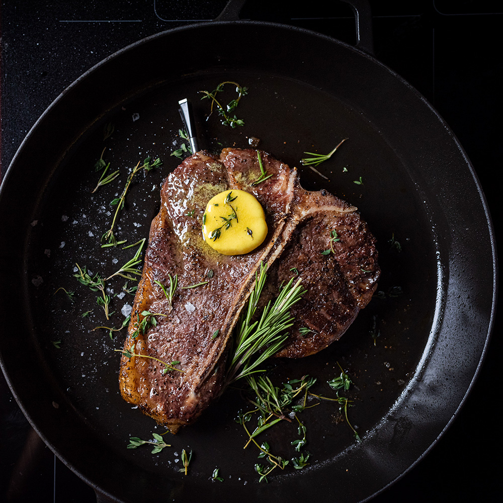 Ein T-Bone-Steak mit Butter und Kräutern gart in einer Gusseisenpfanne.