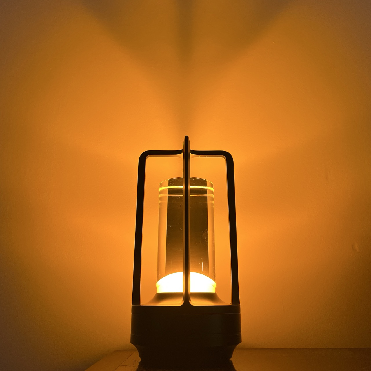 Eine moderne Laterne mit klarem Zylinder und warmem Licht steht auf einer Fläche.