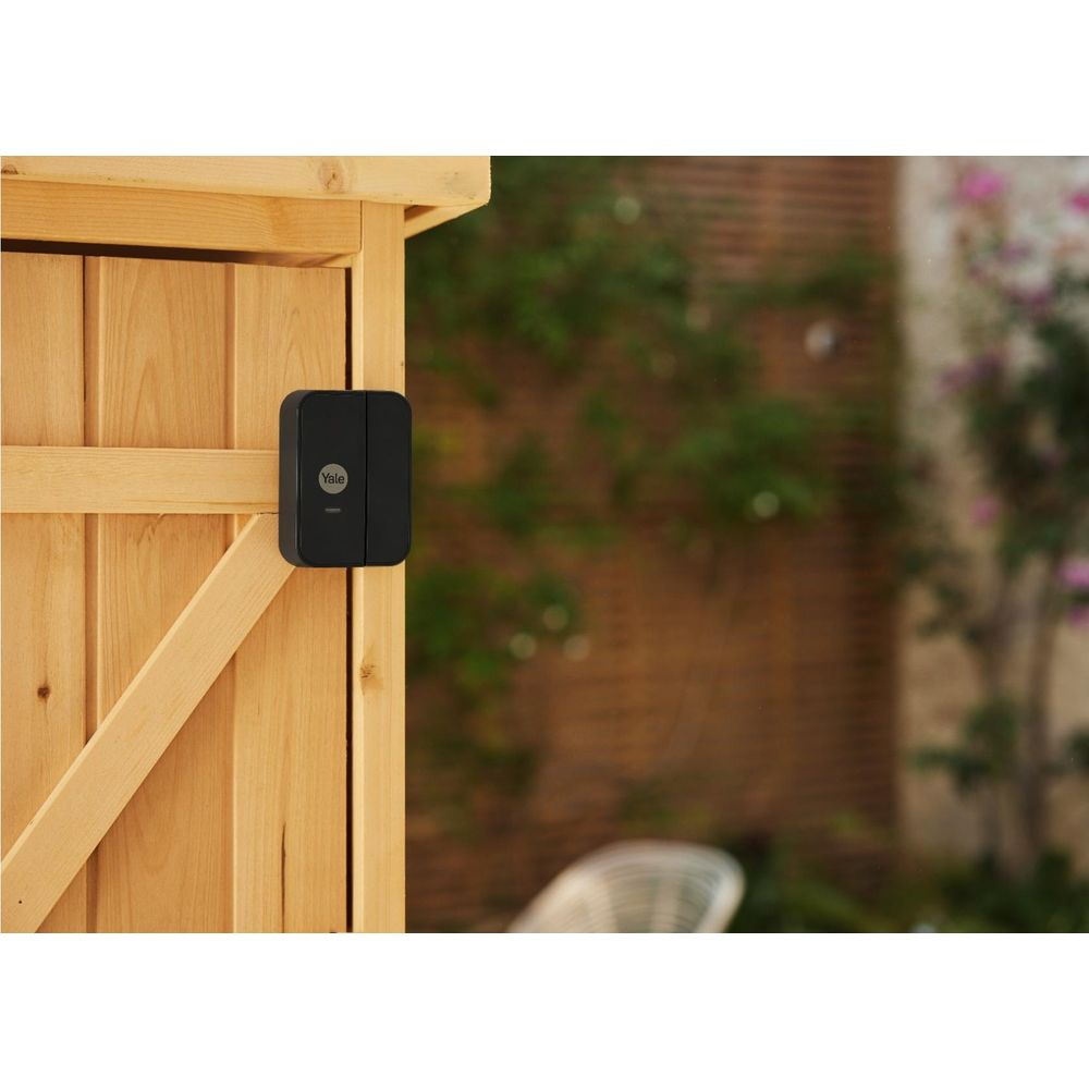Una serratura Yale nera su una porta di legno, con sfondo sfocato.