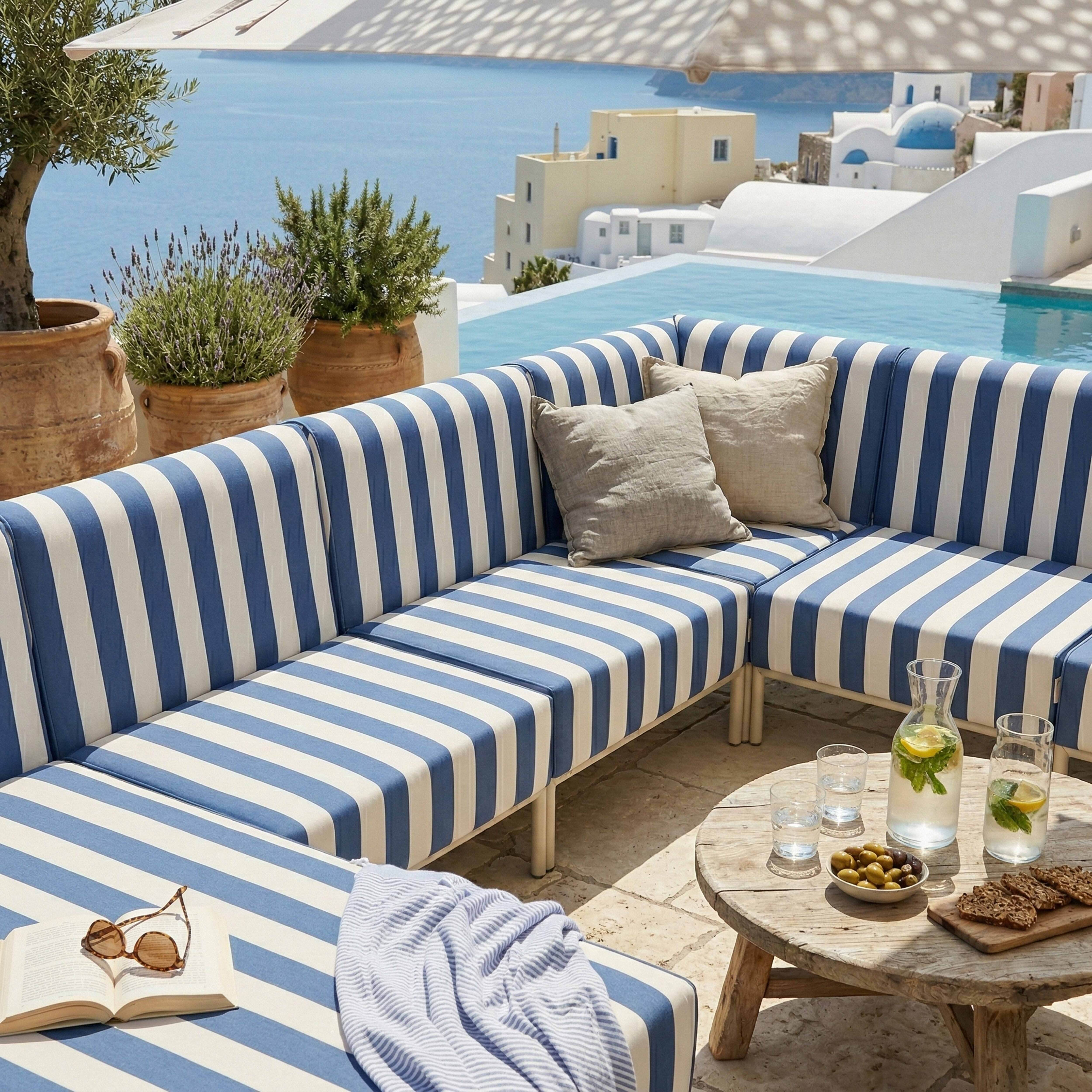 Gestreifte Couch am Pool mit Blick auf das Meer und griechische Architektur.